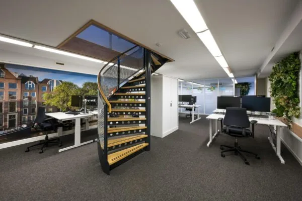 Modern kantoorinterieur aan de Prins Hendrikkade met werkplekken, een wenteltrap en een grote muurprint van Amsterdamse huizen.